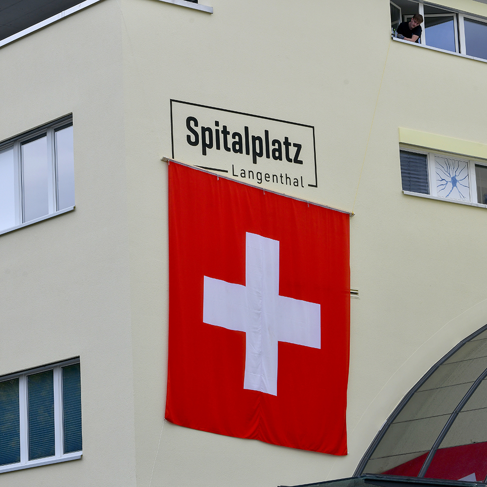 Der Name "Affenplatz" in Langenthal verschwindet. Der Platz heisst wieder "Spitalplatz". Der neue Schriftzug wird enthüllt hinter einer Schweizer Fahne. Bild: Thomas Peter